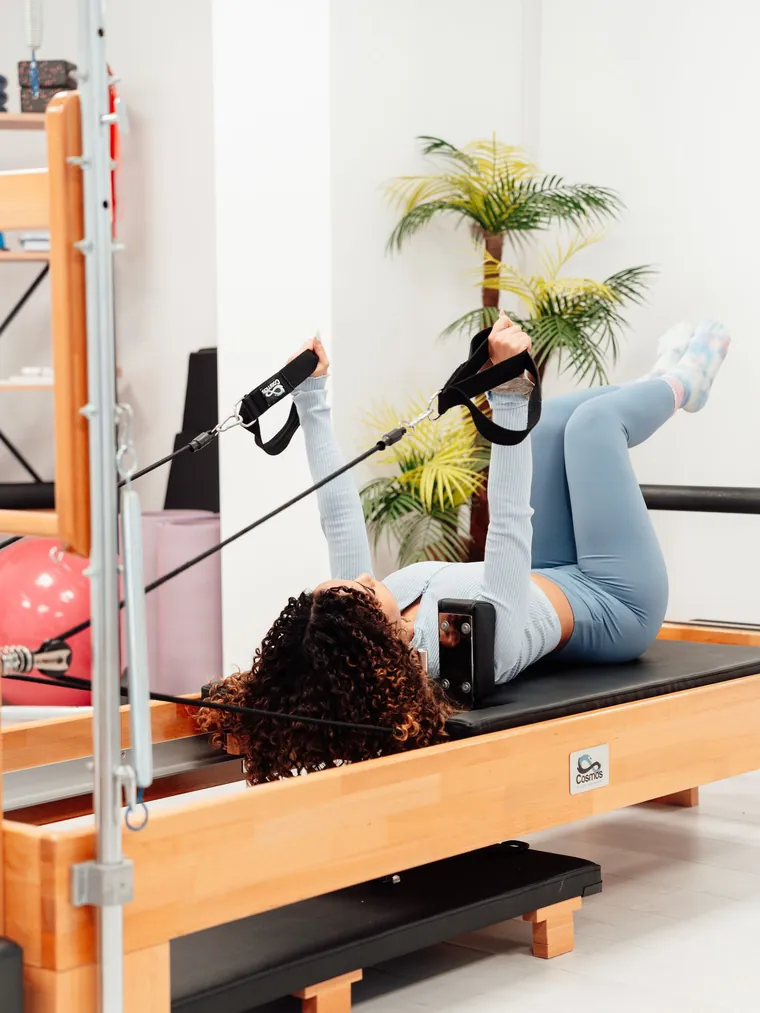 Aluna em exercício no reformer, com faixas nas mãos, durante aula de Pilates fisioterapêutico